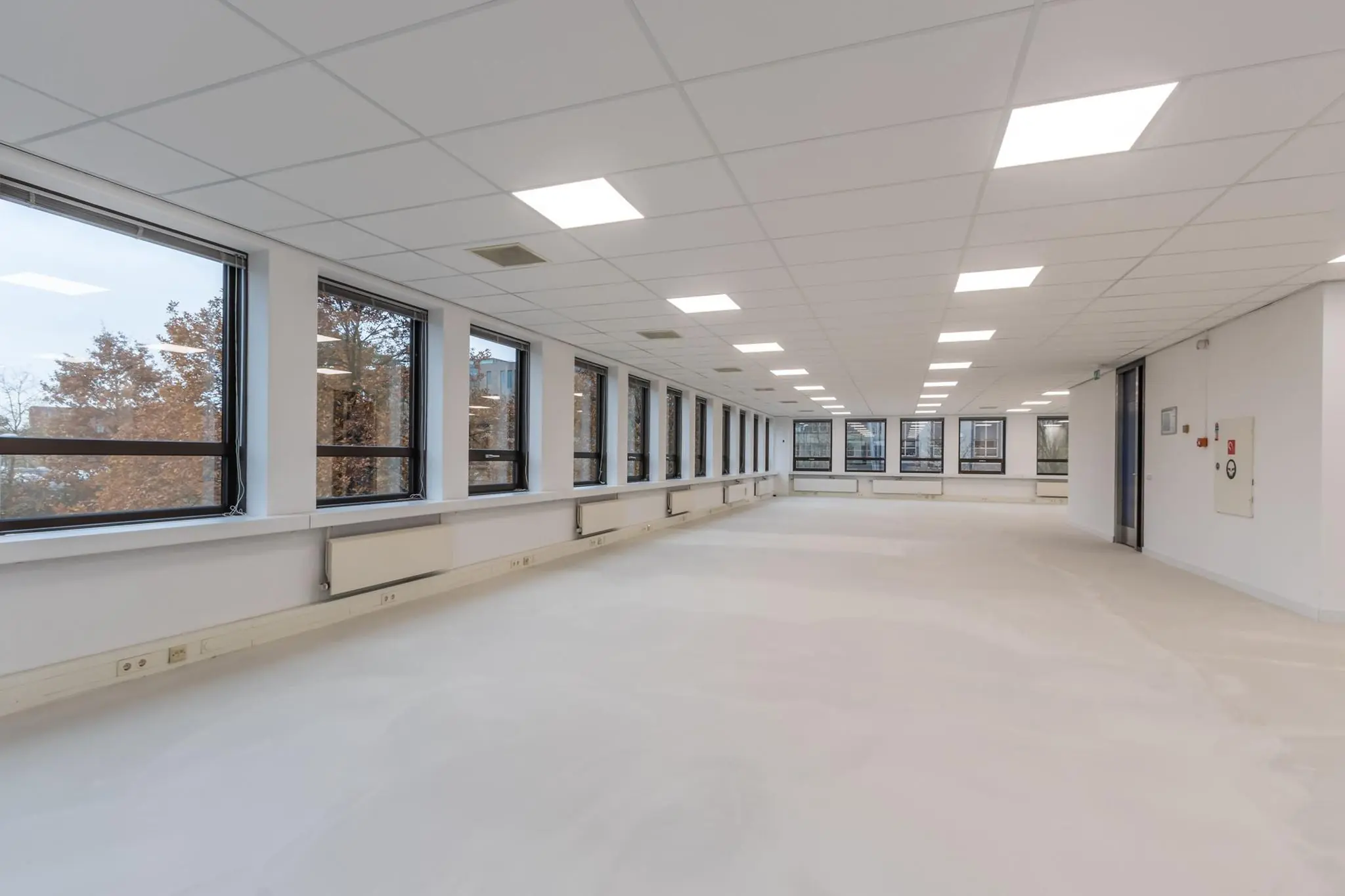 Leeg, modern kantoorruimte met systeemplafond en grote ramen aan één zijde.