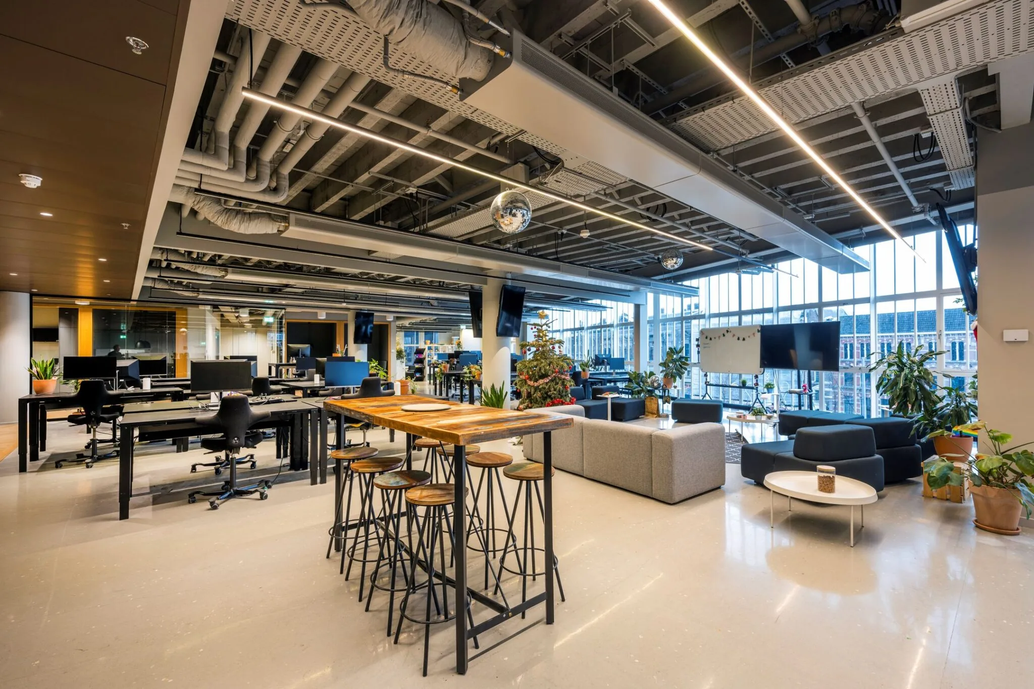 Moderne en open kantooruimte met flexplekken, zithoeken, een hoge tafel met krukken en een kerstboom in een lichte, industriële setting.