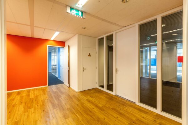 Moderne kantoorhal aan de Braillelaan met houten vloer, feloranje muur en meerdere deuren naar vergaderruimtes.