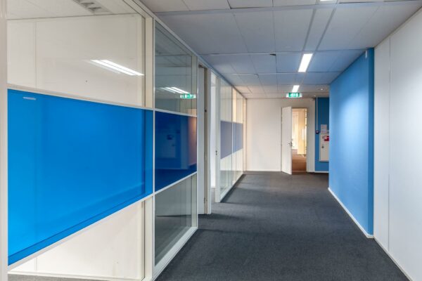 Hal met glazen wanden en blauwe panelen in kantoorpand aan de Braillelaan.