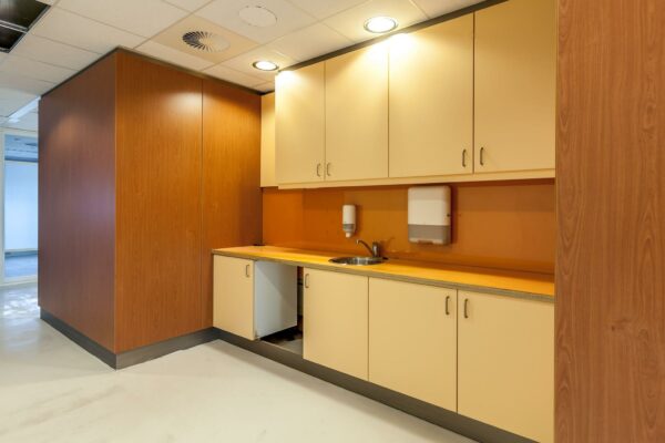 Keukenblok met beige kastjes en oranje achterwand in kantoorpand aan de Braillelaan.
