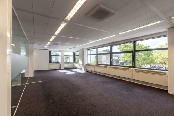 Lichte, lege kantoorruimte aan de Braillelaan met grote ramen en donker tapijt.