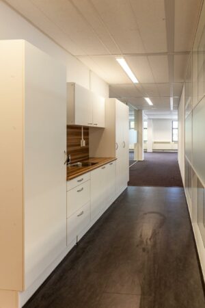 Kleine pantry met witte kasten en een houten werkblad in een gang van een kantoorpand aan de Braillelaan.