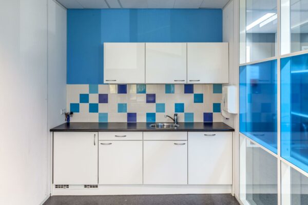 Kleine pantry met witte keukenkastjes, een zwart aanrechtblad en een witte tegelwand met blauwe accenten aan de Braillelaan.