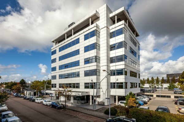 Wit kantoorgebouw aan de Braillelaan met parkeerplaatsen en geparkeerde auto’s op een zonnige dag.