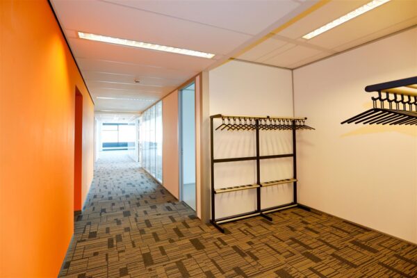 Moderne kantoorhal op het Bogaardplein met oranje muur, garderobe en tapijtvloer.
