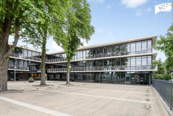 Modern kantoorgebouw aan de Rijksstraatweg met glazen gevels en een ruime, betegelde parkeervoorzijde.