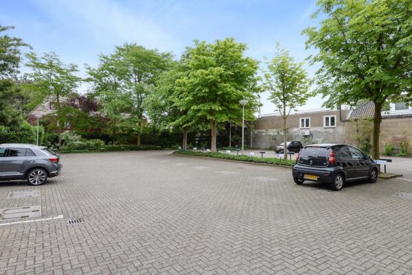 Ruim opgezette parkeerplaats aan de Rijksstraatweg, omringd door bomen en woonhuizen.