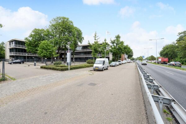 Kantoorgebouw aan de Rijksstraatweg met geparkeerde auto's langs de weg en een drukke rijbaan rechts.