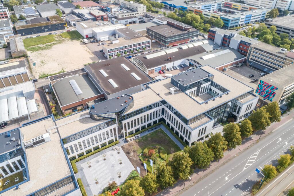 Luchtfoto van een modern kantoorgebouw aan de Volmerlaan in een bedrijventerrein met omliggende bedrijfsgebouwen en parkeerplaatsen.