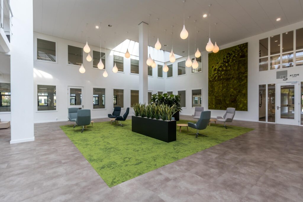 Moderne en lichte kantoorlobby aan de Volmerlaan met groene accenten, designstoelen en hangende verlichting.
