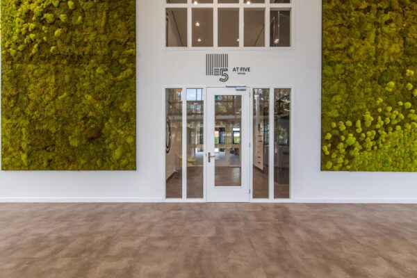 Ingang van het kantoorgebouw "At Five" aan de Volmerlaan met grote groene moswanden aan weerszijden van een glazen deur.