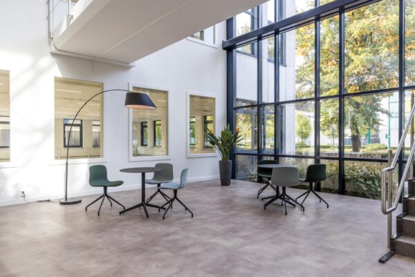 Moderne en lichte ontvangstruimte in kantoorpand aan de Volmerlaan met zitjes, grote ramen en een design vloerlamp.