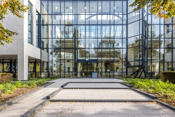 Moderne glazen entree van kantoorgebouw aan de Volmerlaan 5 met symmetrische architectuur en omliggend groen.