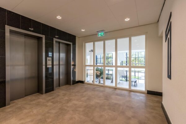 Moderne liftlobby in een kantoorgebouw aan de Volmerlaan met twee liften en uitzicht op een open, licht atrium.