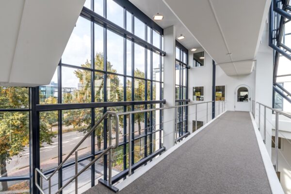 Licht en modern interieur van een kantoorgebouw aan de Volmerlaan met een loopbrug en grote glazen gevelramen.