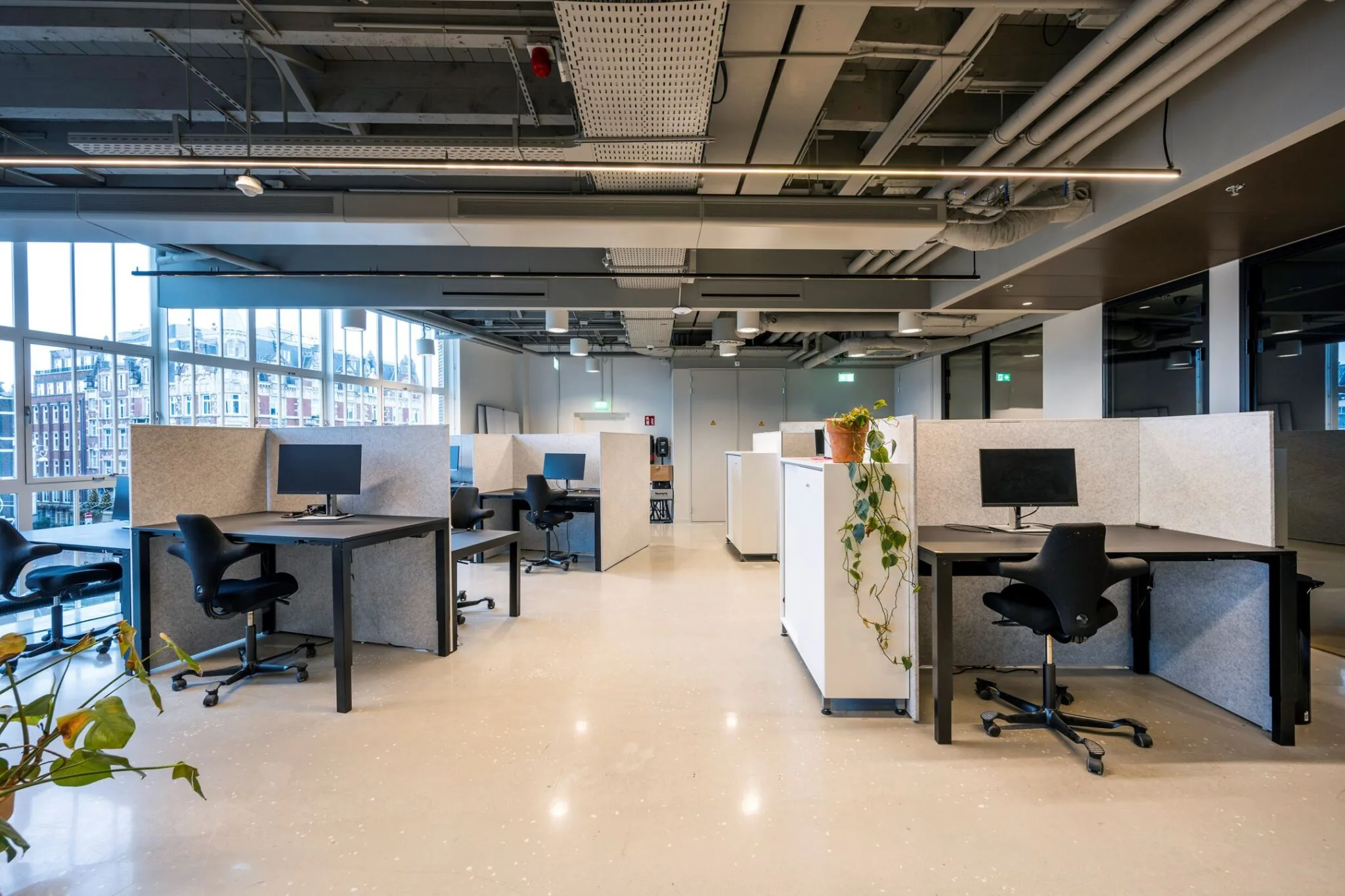 Moderne, open kantoorruimte met werkplekken voorzien van bureaus, beeldschermen, ergonomische stoelen en scheidingspanelen.