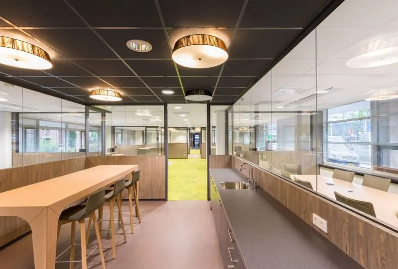 Moderne kantoorruimte aan het Spui met glazen wanden, houten meubilair en een groene vloerbedekking in de gang.