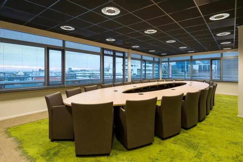 Vergaderruimte met een ovale tafel en rondom geplaatste stoelen in het Spui-gebouw, met uitzicht op de stad.