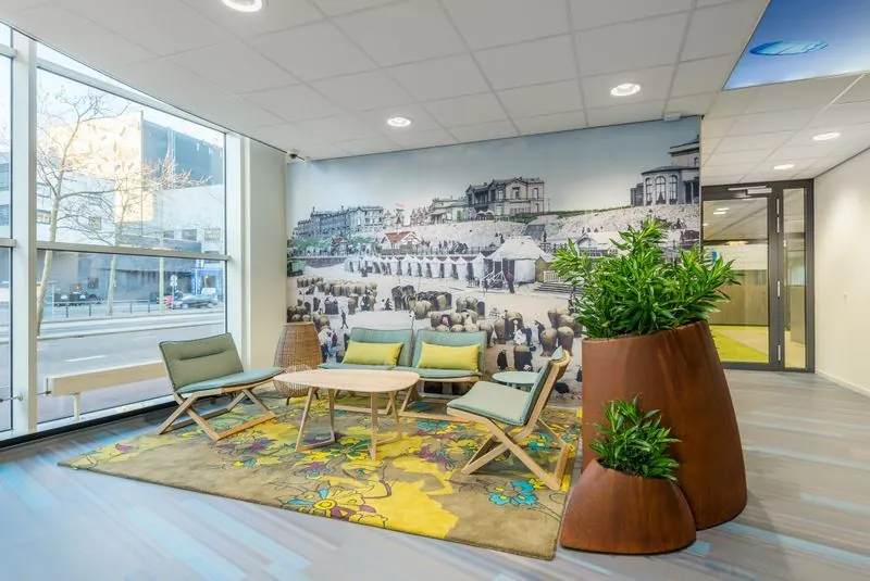 Moderne wachtruimte met kleurrijk vloerkleed, planten en een muurfoto van het historische Spui in Den Haag.