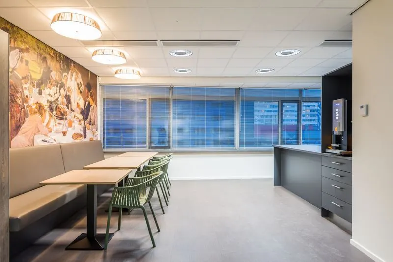 Moderne, lichte bedrijfskantine met zitplaatsen, een koffieautomaat en een muurschildering van het Spui.