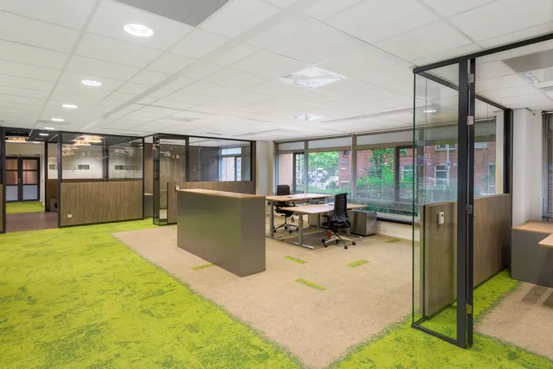 Modern kantoorpand aan het Spui met glazen wanden, groene vloerbedekking en werkplekken met uitzicht op buiten.