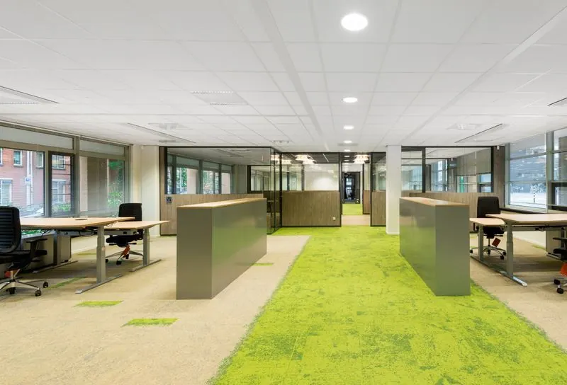Moderne kantoorruimte aan het Spui met open werkplekken, glazen wanden en opvallende groene vloerbedekking.