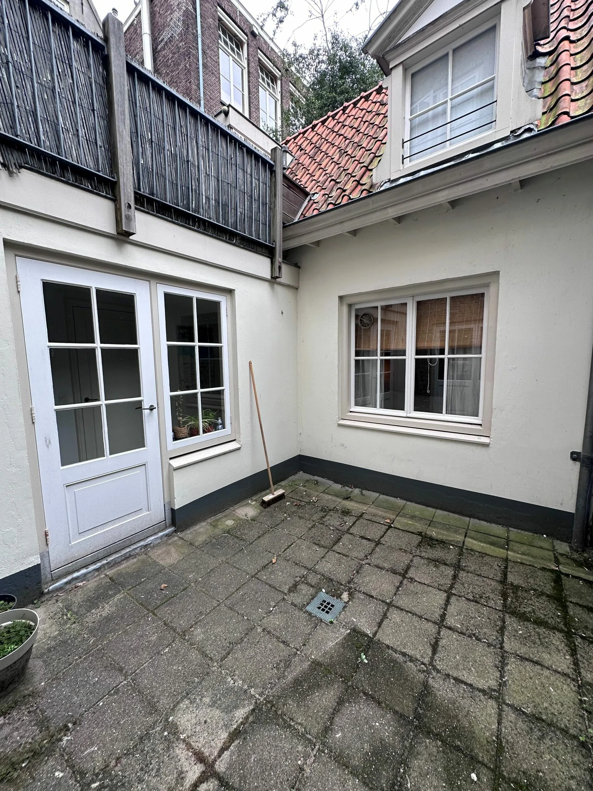 Kleine, betegelde binnenplaats met witte muren, ramen, deuren en een bezem tegen de muur.