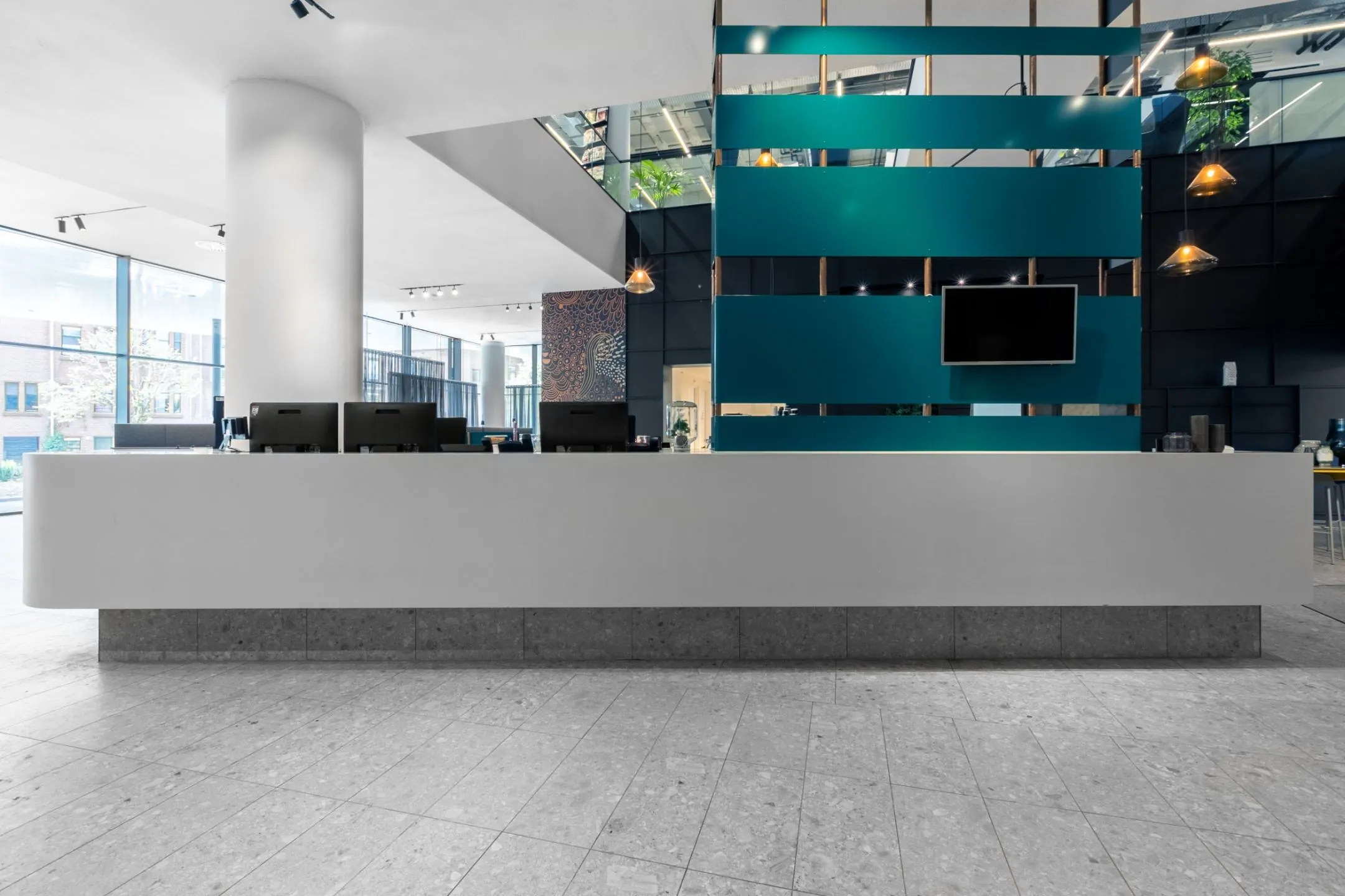 Moderne receptiebalie in een strak vormgegeven kantoorruimte met turquoise wandaccenten en computers.
