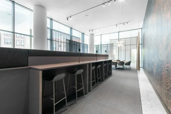 Moderne, open kantoorruimte met hoge ramen, lange werktafel en vergadertafel in een lichte en stijlvolle inrichting.