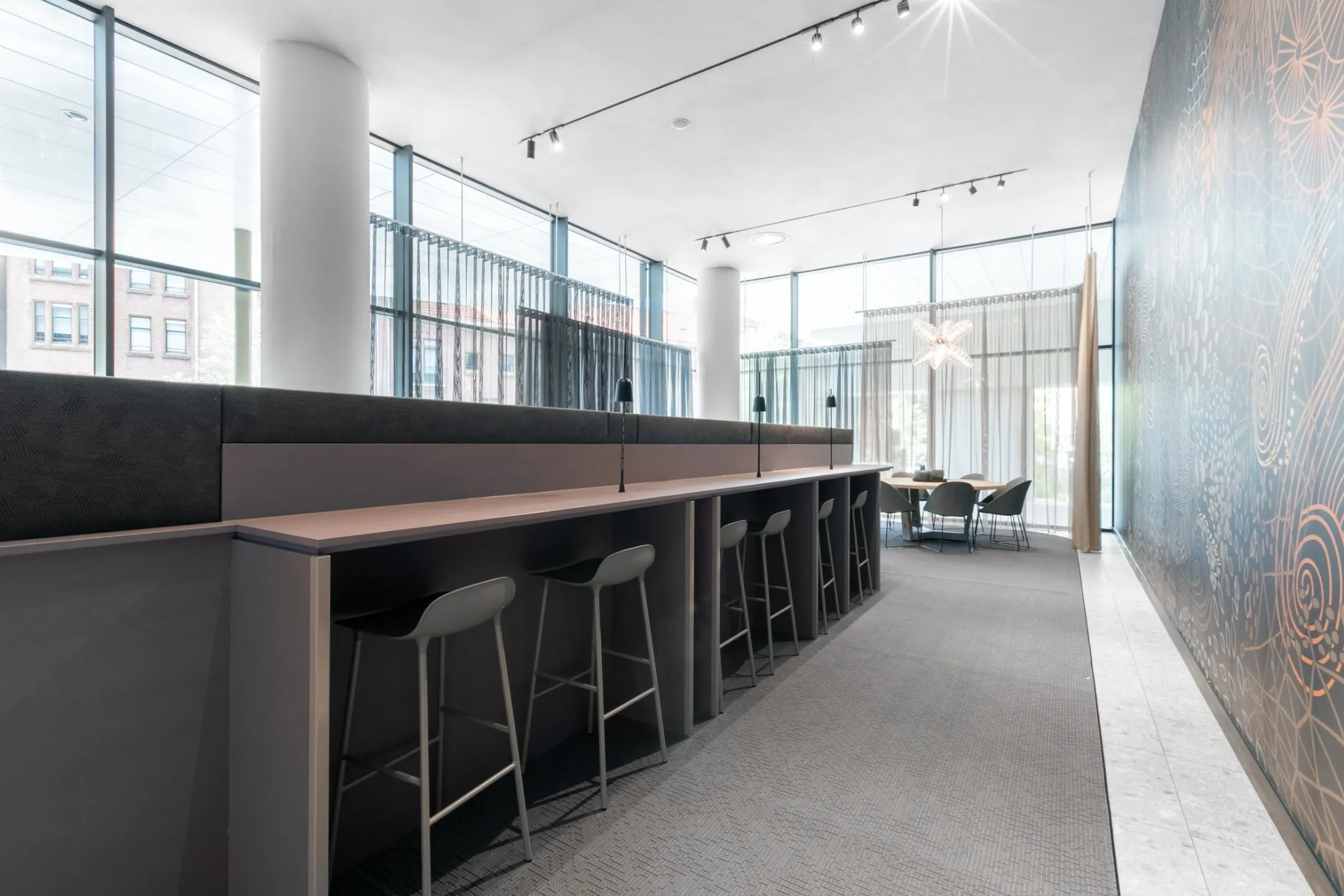 Moderne, open kantoorruimte met hoge ramen, lange werktafel en vergadertafel in een lichte en stijlvolle inrichting.