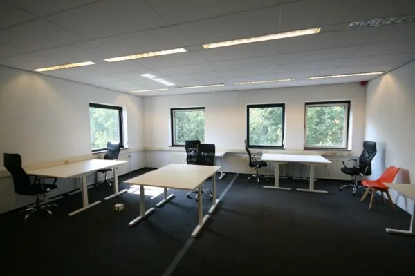 Kantoorruimte aan de Corkstraat met meerdere bureaus, bureaustoelen en grote ramen die uitkijken op groen.