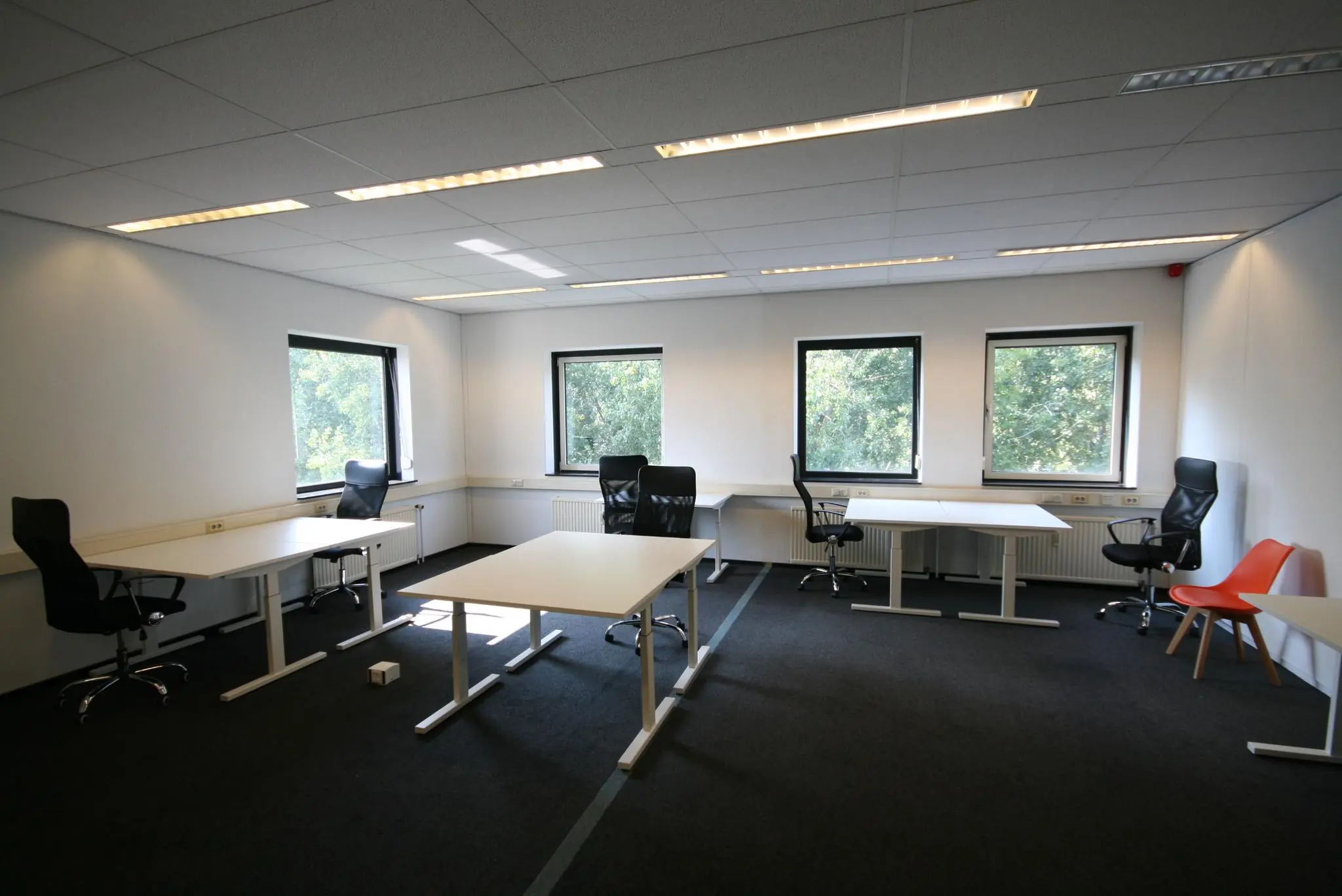 Kantoorruimte aan de Corkstraat met meerdere bureaus, bureaustoelen en grote ramen die uitkijken op groen.