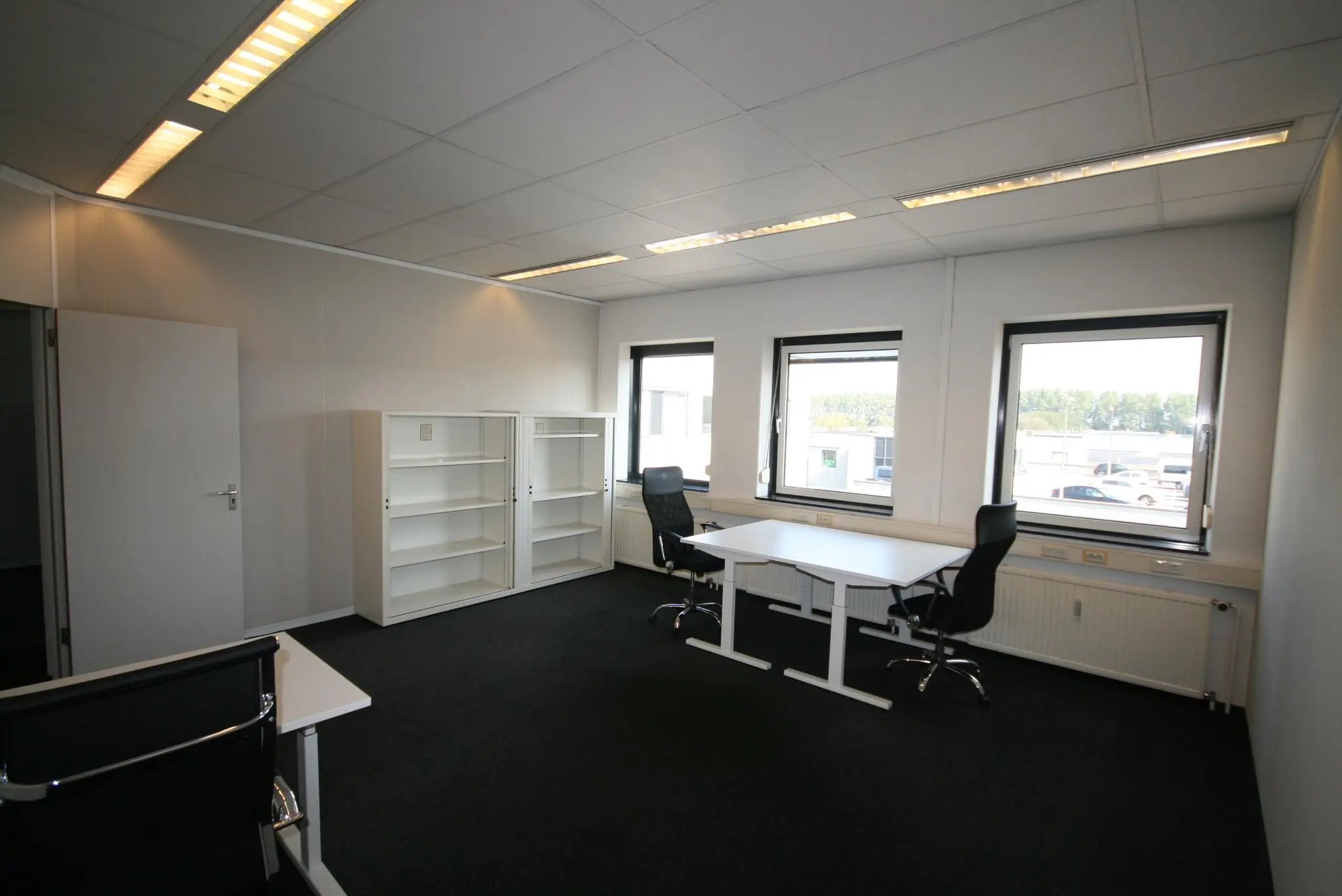 Licht en modern kantoor op de Corkstraat met twee bureaus, zwarte bureaustoelen en witte kasten.