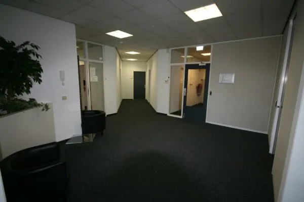 Hal met donkere deuren, glazen kantoorwanden, zwarte stoelen en een plant in een bedrijfsgebouw aan de Corkstraat.