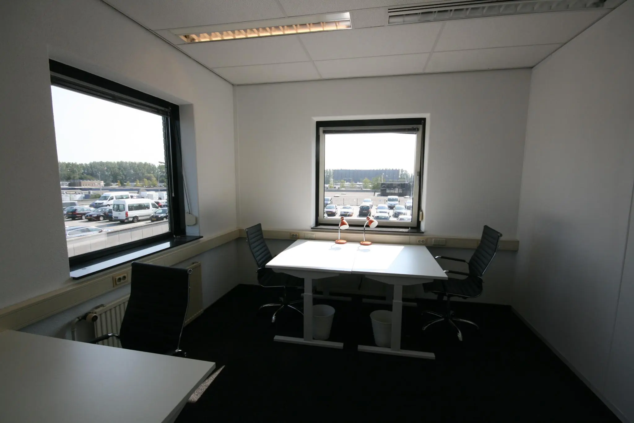 Kleine kantoorruimte aan de Corkstraat met twee bureaus, vier stoelen en uitzicht op een parkeerplaats.