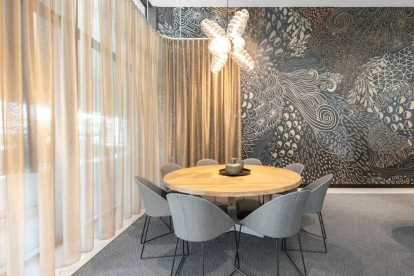 Moderne vergaderruimte met ronde houten tafel, grijze stoelen en een opvallende wand met abstracte kunst.