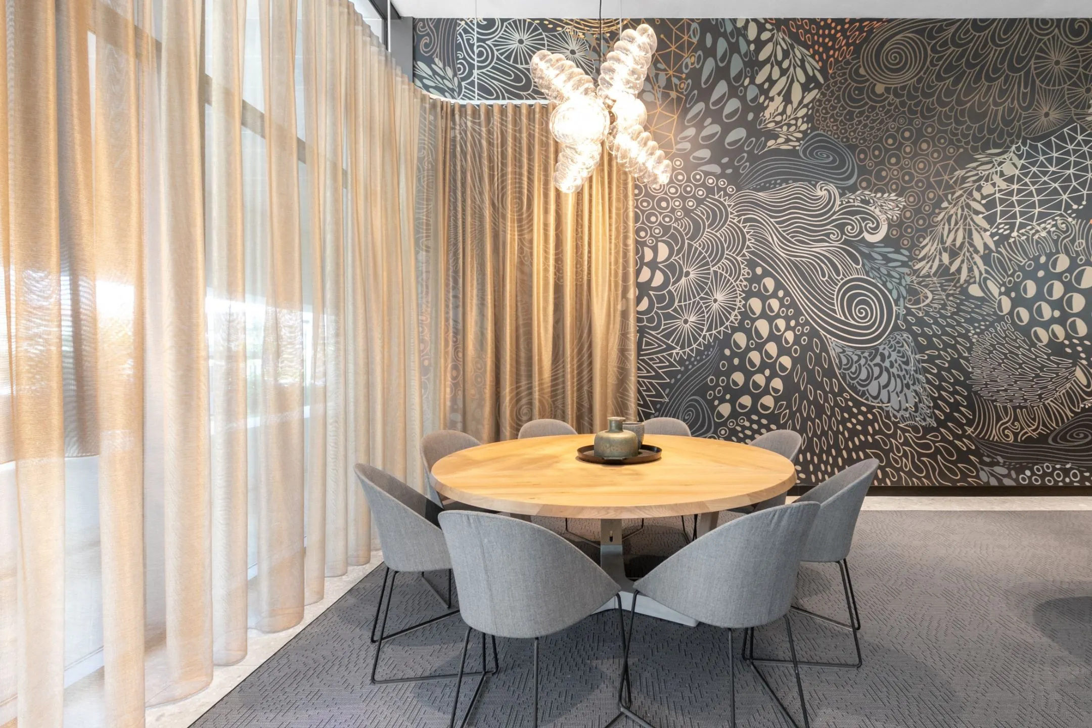 Moderne vergaderruimte met ronde houten tafel, grijze stoelen en een opvallende wand met abstracte kunst.