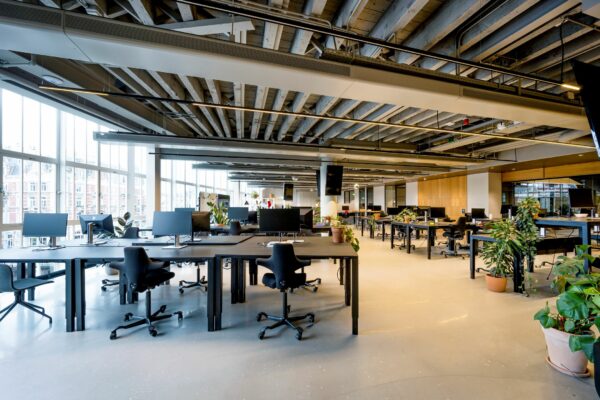 Moderne open kantoorruimte met bureaus, computers en veel groenplanten.