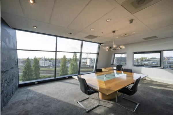 Vergaderruimte met moderne houten tafel en grote ramen met uitzicht op het spoor bij Rietlandpark.