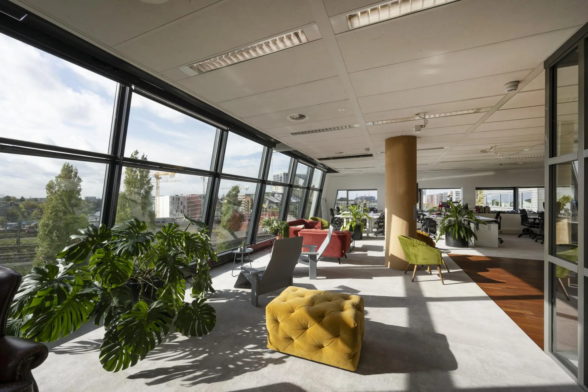 Moderne kantoorruimte in Rietlandpark met grote ramen, veel daglicht, kleurrijke zitmeubels en groene planten.