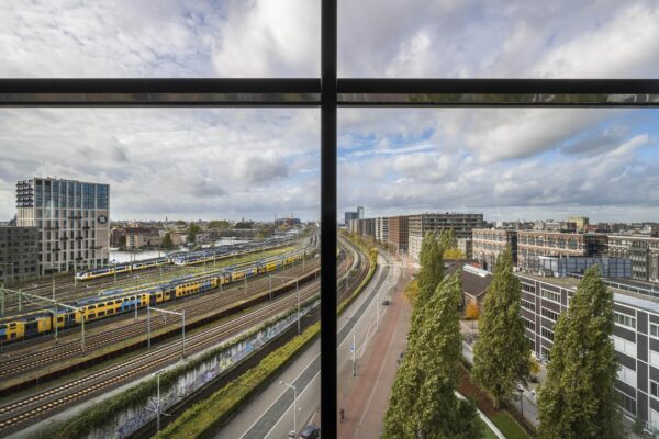Uitzicht op het Rietlandpark in Amsterdam met spoorlijnen, passerende treinen en omliggende moderne bebouwing.