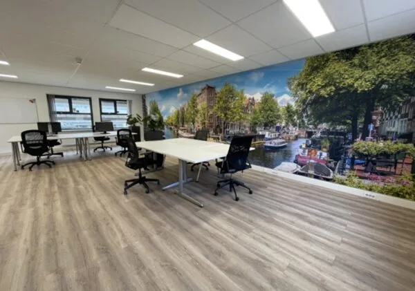 Moderne kantoorruimte aan de Arlandaweg met werkplekken, laminaatvloer en een muurfoto van een Amsterdams grachtenbeeld.
