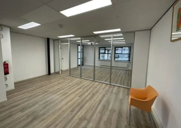 Lichte, lege kantoorruimte aan de Arlandaweg met glazen tussenwand, houten vloer en een oranje stoel.