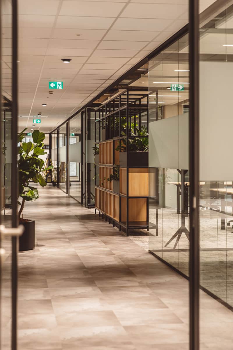 Een moderne kantoorhal met glazen wanden, planten en houten elementen.