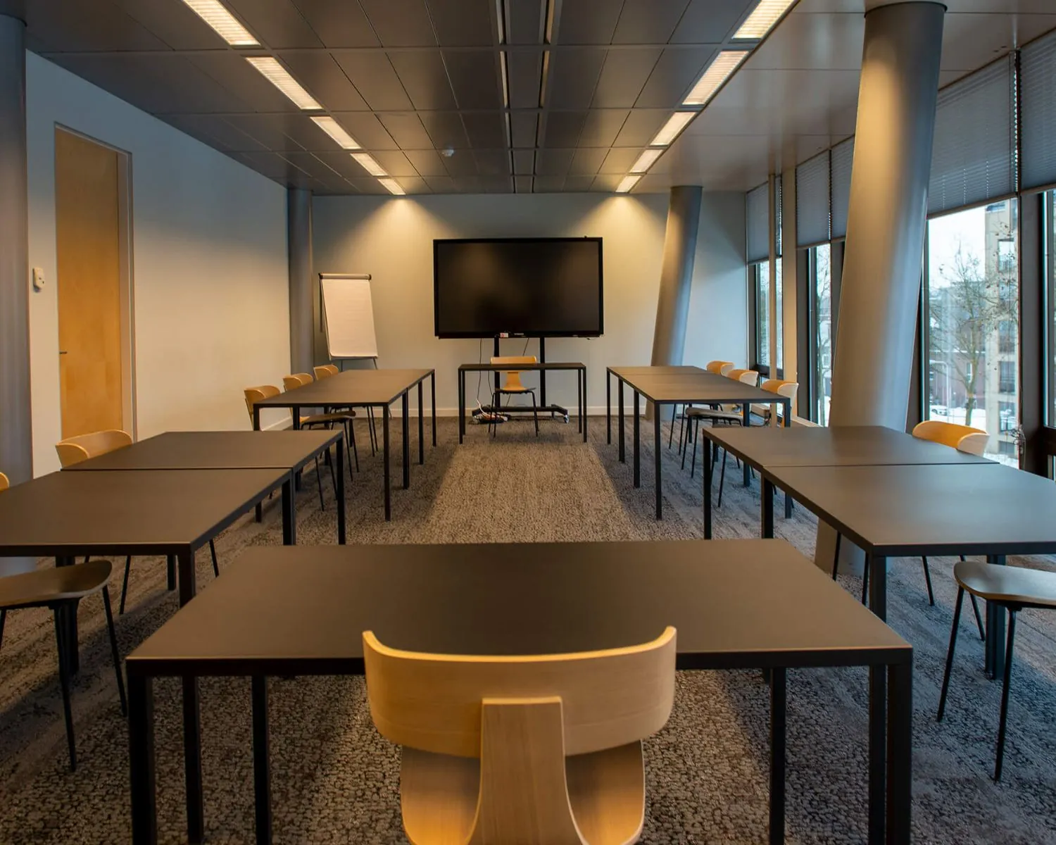 Vergaderruimte A-Meeting-05 met opstelling in U-vorm, voorzien van tafels, stoelen, een flip-over en een groot presentatiescherm.