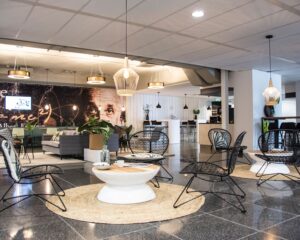 Moderne lounge- en zitruimte met zwarte stoelen, ronde tafels en een muurschildering van Albert Einstein op de achtergrond.