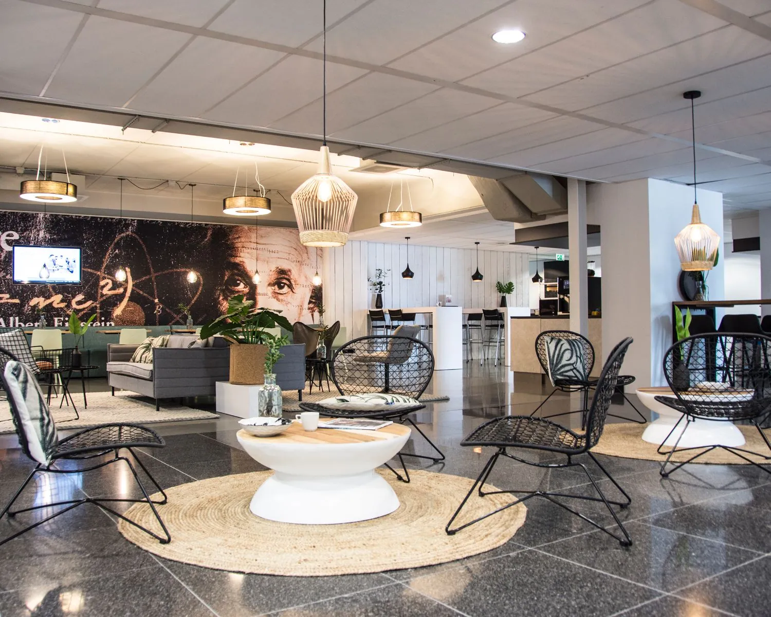 Moderne lounge- en zitruimte met zwarte stoelen, ronde tafels en een muurschildering van Albert Einstein op de achtergrond.