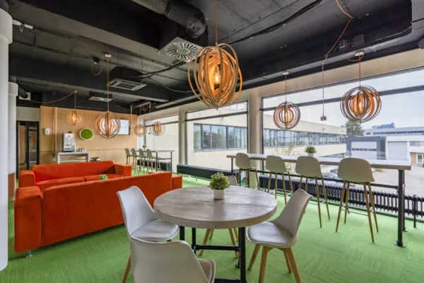 Moderne algemene ruimte in Aalsmeer met felgroen tapijt, oranje bank, houten verlichting en grote ramen.
