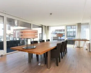 Moderne vergaderruimte met grote houten tafel, designlampen en uitzicht op de Dr. Lelykade in Den Haag.